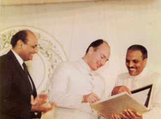 Mawlana Hazar Imam receives the Charter of AKU from President General Mohammad Zia-ul-Haq as Shamsh Kassim-Lakha, founding President of AKU, applauds. March 16, 1983. Photo: Hidayat